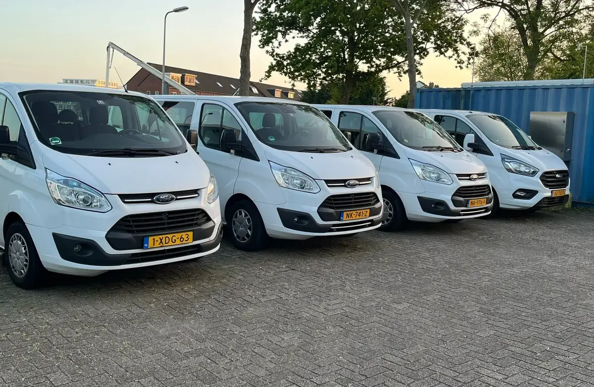 Vier witte personenbussen met gele kentekens