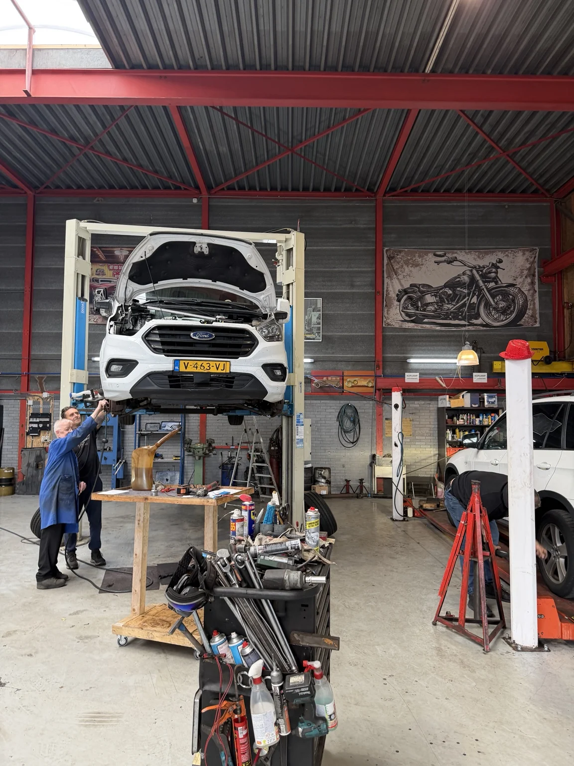 Monteurs werken aan een auto op de brug in de garage van De Roo